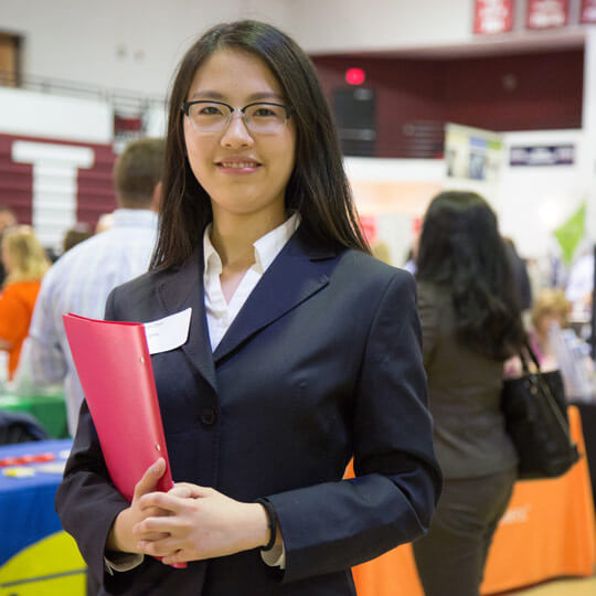 a student wearing glasses and a dark blazer smiles at the camera at the career fair