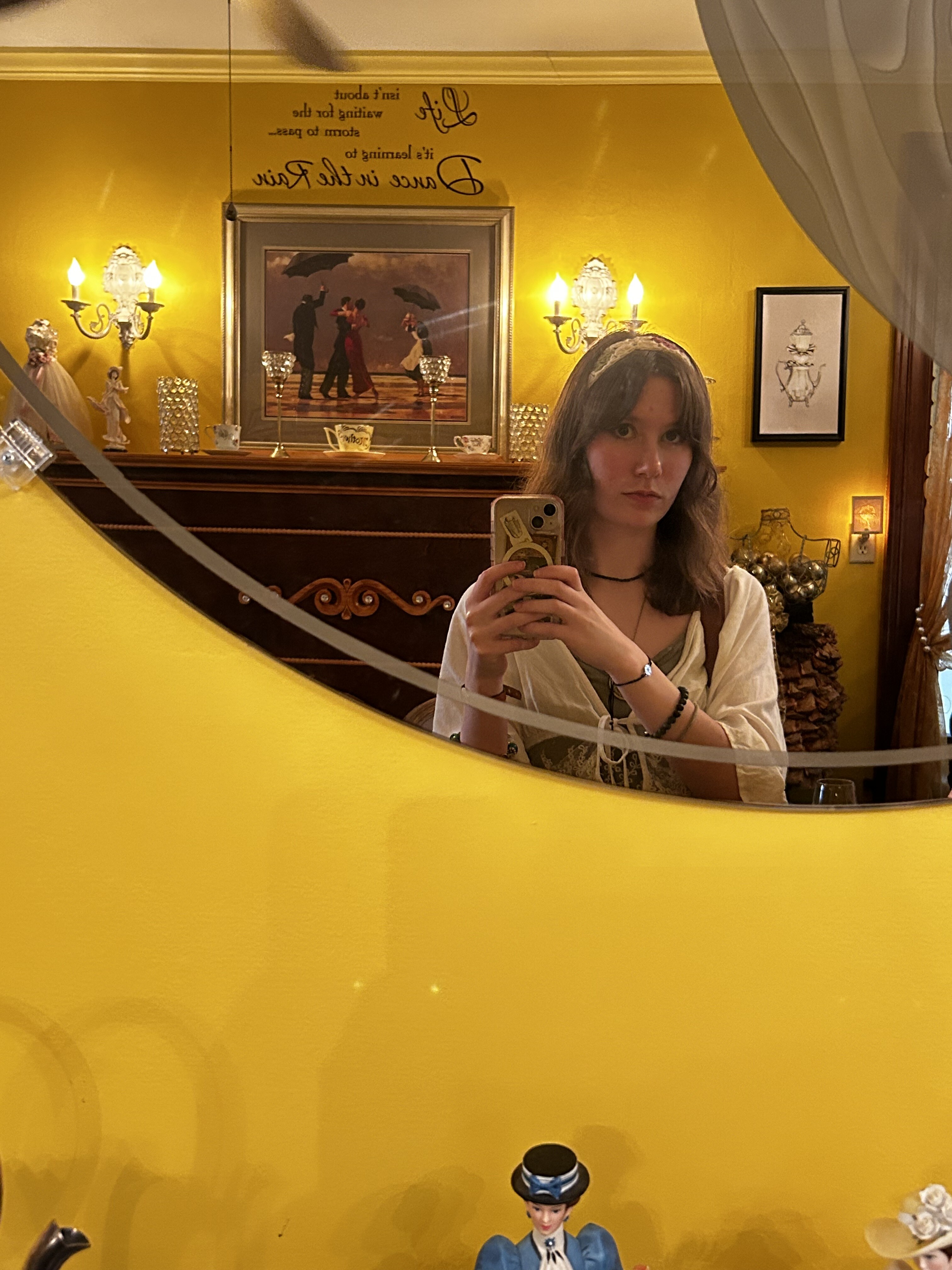 Student looking in a mirror on a yellow wall, holding a phone